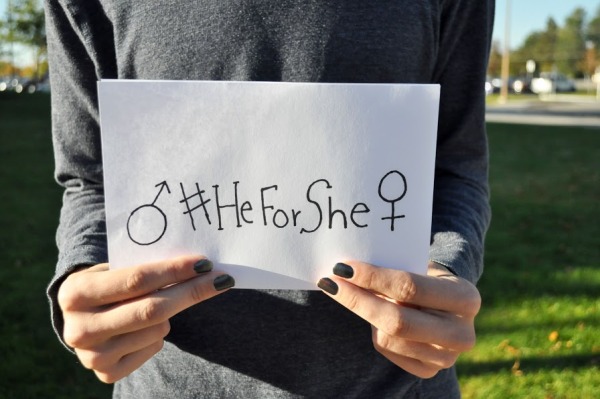 A male advocate for gender equality holds a sign tagged with #HeforShe, supporting the organization.