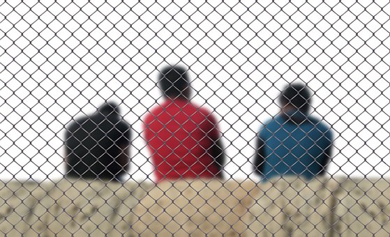 Three men sit behind a fence in order to symbolize deportation.