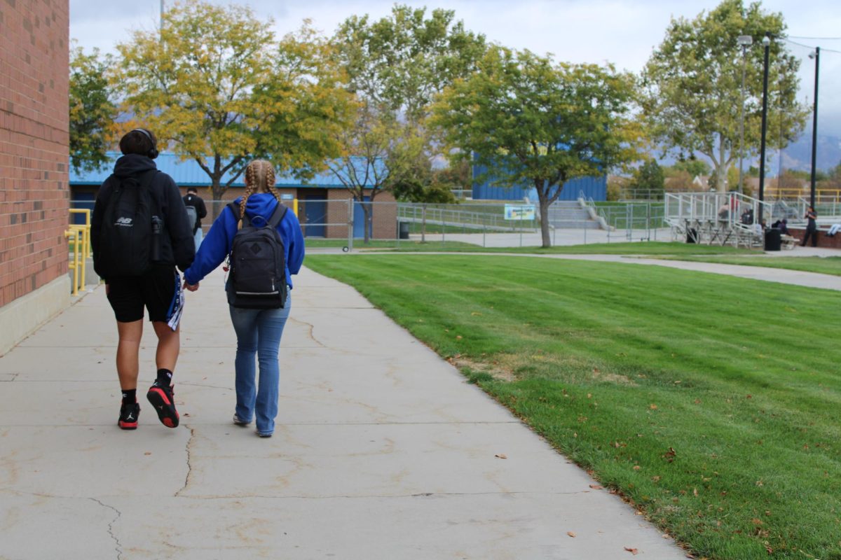 Two students walking while holding hands on school grounds.